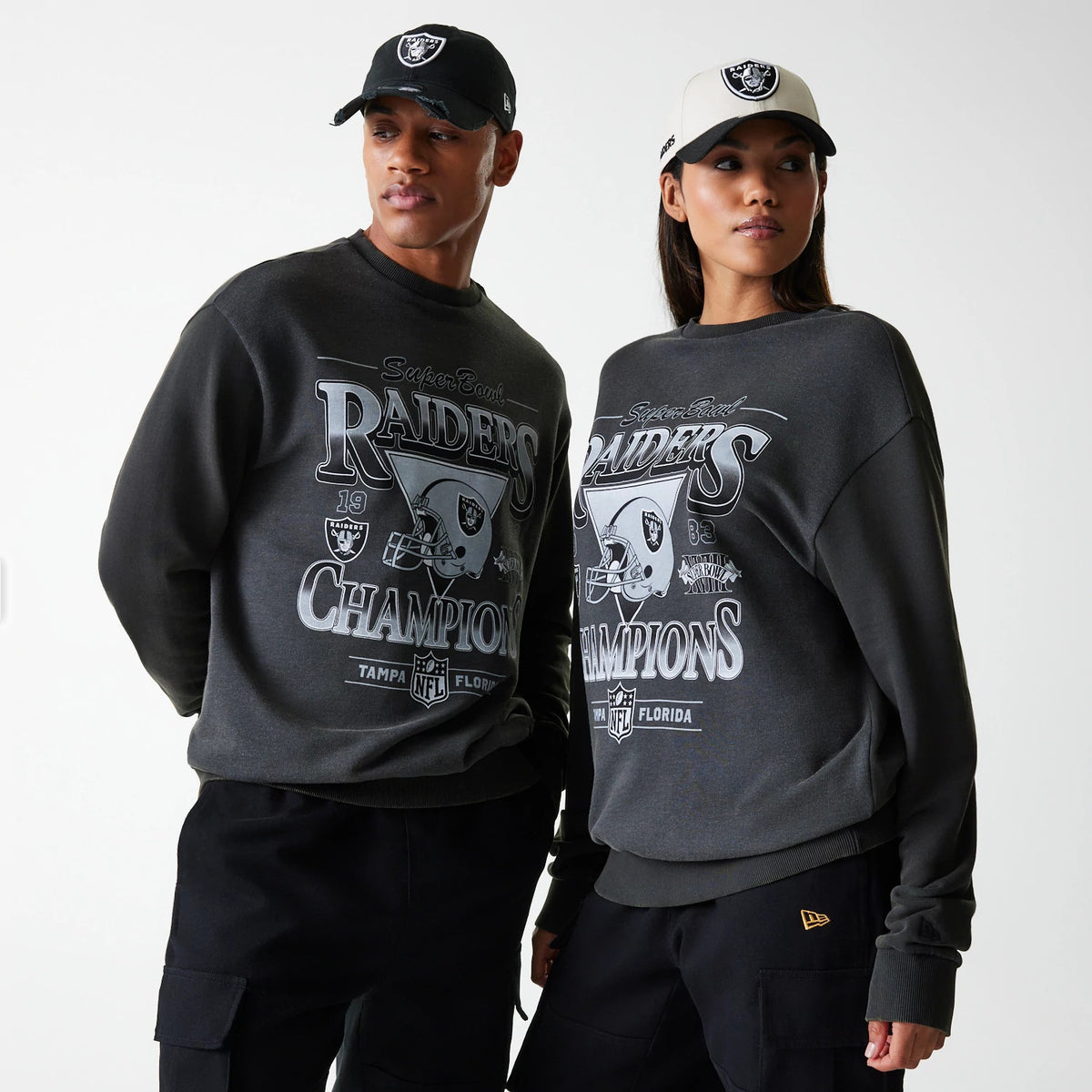 New Era Las Vegas Raiders NFL Washed Super Bowl Grey Oversized Crew Neck Sweater, on models wearing black and white Raiders caps, featuring large front graphics with Super Bowl Champions text and Raiders logo.
