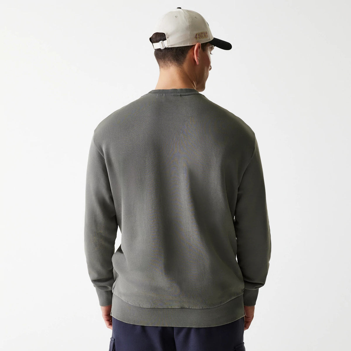 New Era San Francisco 49ers NFL Washed Super Bowl Grey Oversized Crew Neck Sweater, back view on a model wearing a cap, showing the relaxed fit and ribbed hem of the grey sweater against plain trousers.
