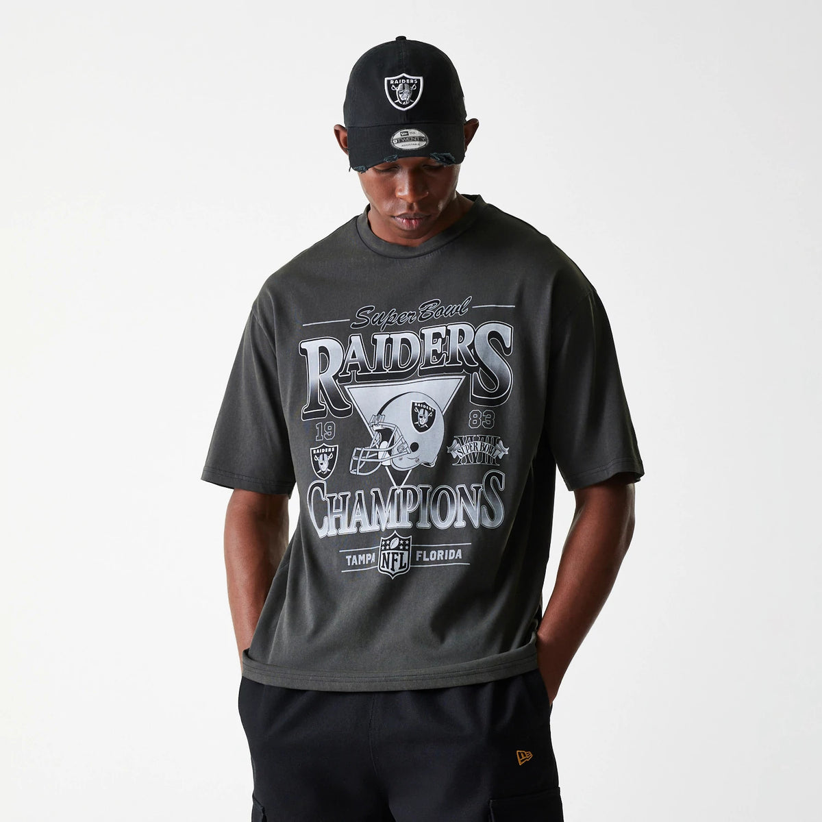 New Era Las Vegas Raiders NFL Washed Super Bowl Grey Oversized T-Shirt, on-model view showing the bold printed front design with Super Bowl Raiders Champions lettering and team logos, paired with a black cap featuring a raised Raiders logo.