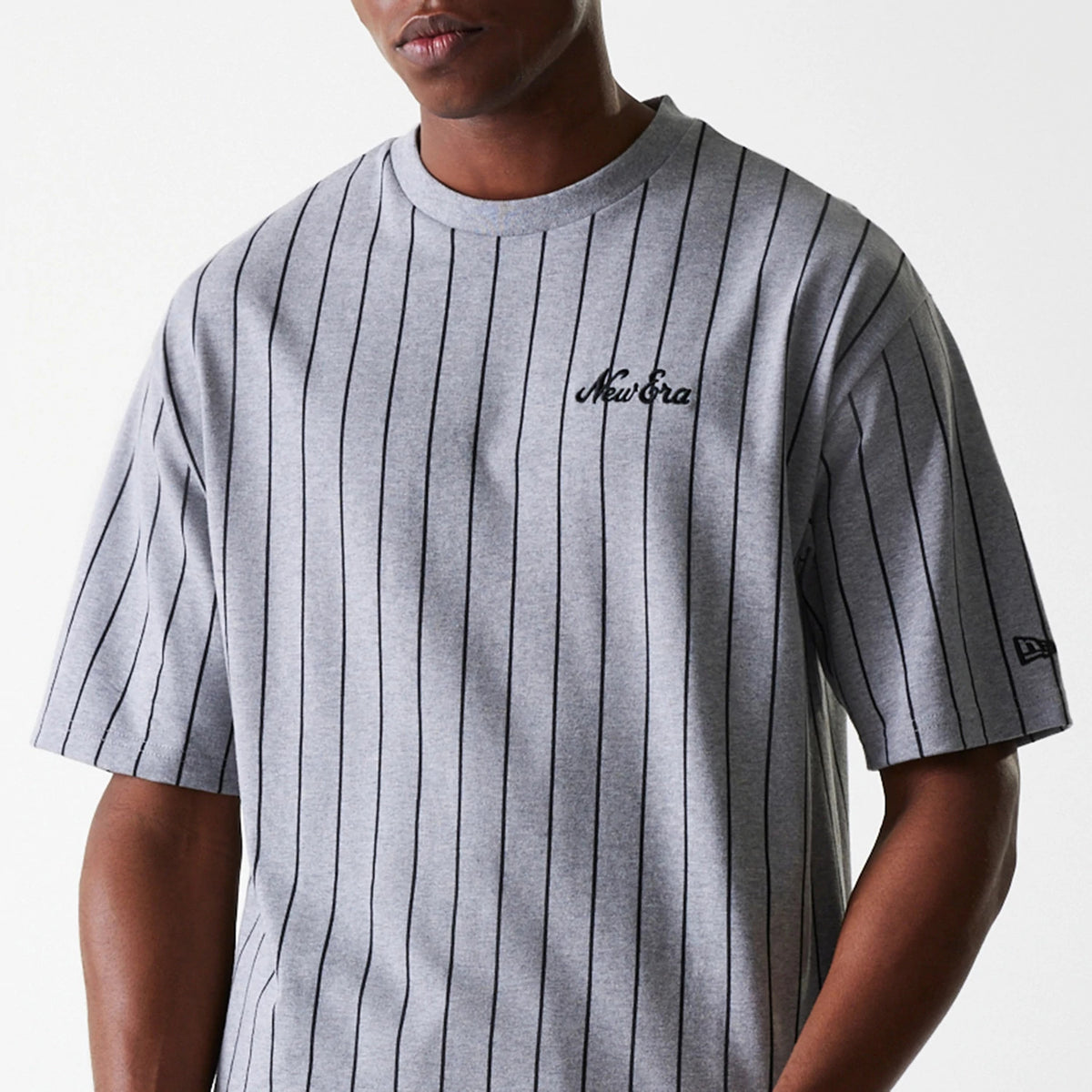 New Era Pinstripe Pastel Grey Oversized T-Shirt, front view showing vertical black pinstripes on a grey fabric, an embroidered New Era logo on the chest, and another logo on the lower sleeve.