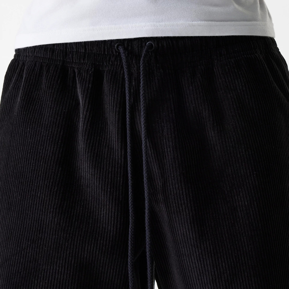 New Era Cord Black Shorts, front view showing the ribbed texture and black drawstring closure at the elasticated waistband, complemented by a plain white top above.