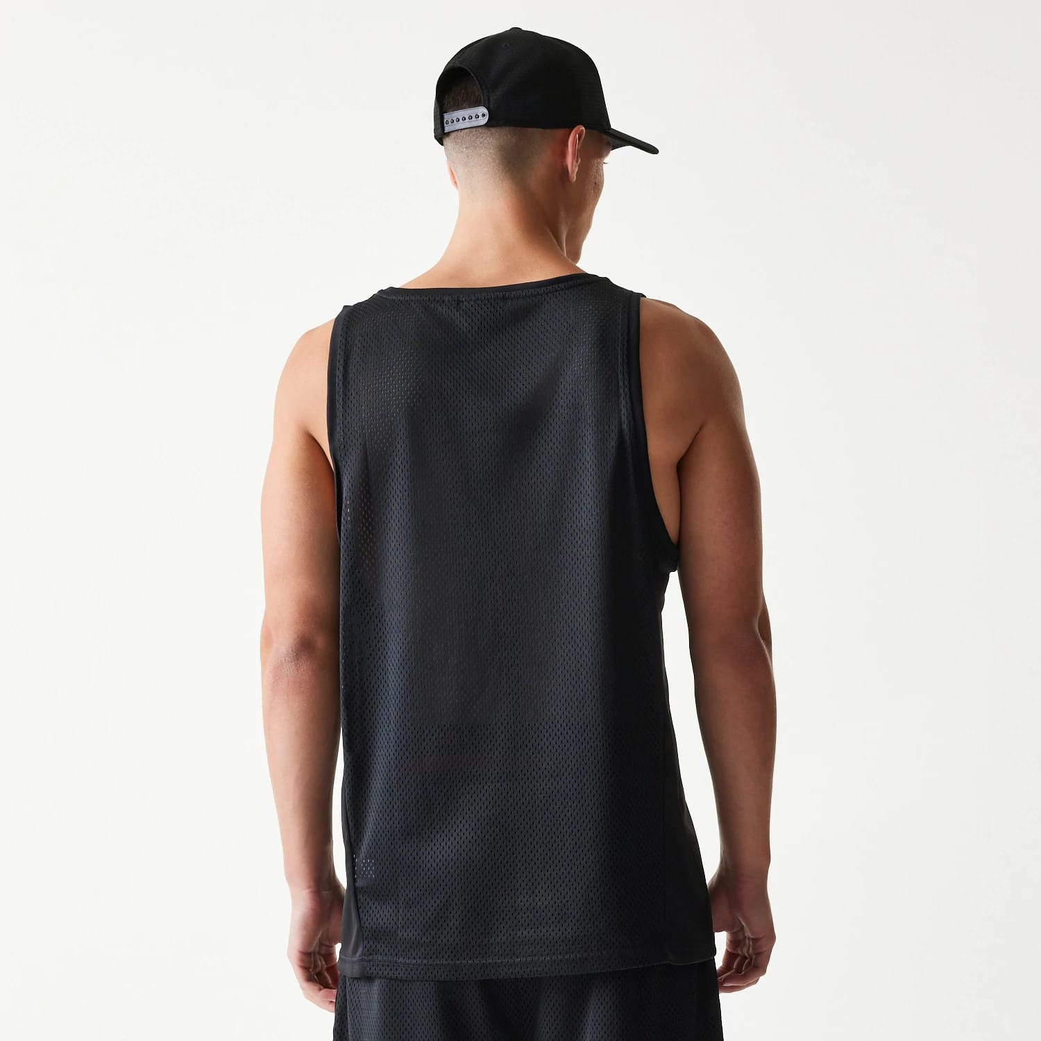 New Era Mesh Black Mesh Vest, back view on a model wearing the vest with matching shorts, showing the sleeveless design and textured mesh fabric, complemented by a black cap with an adjustable snapback closure.