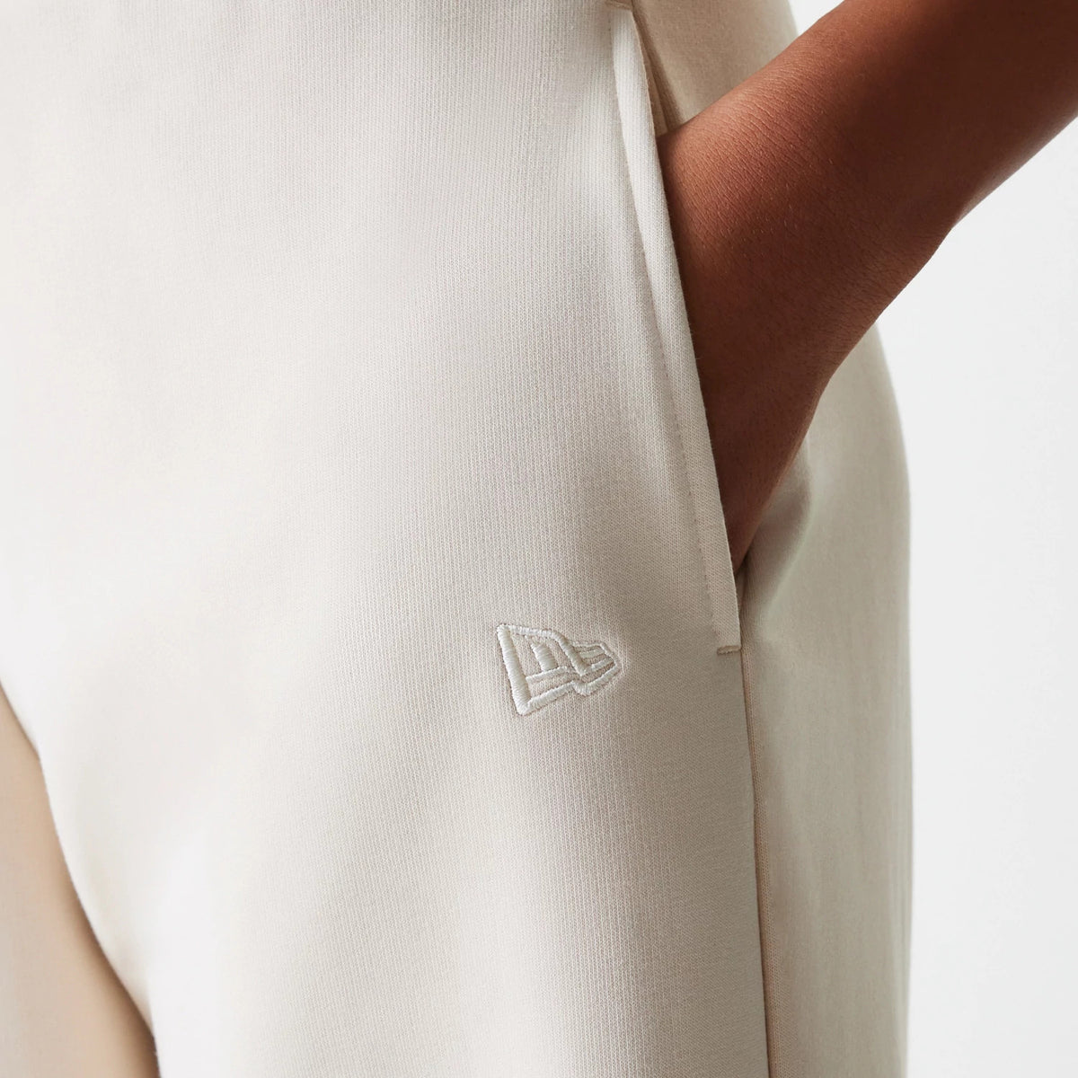 New Era LA Dodgers Womens MLB Tonal Light Beige Straight Leg Joggers, close-up showing a side pocket detail with a white embroidered New Era flag logo below the pocket seam, on a soft light beige fabric.