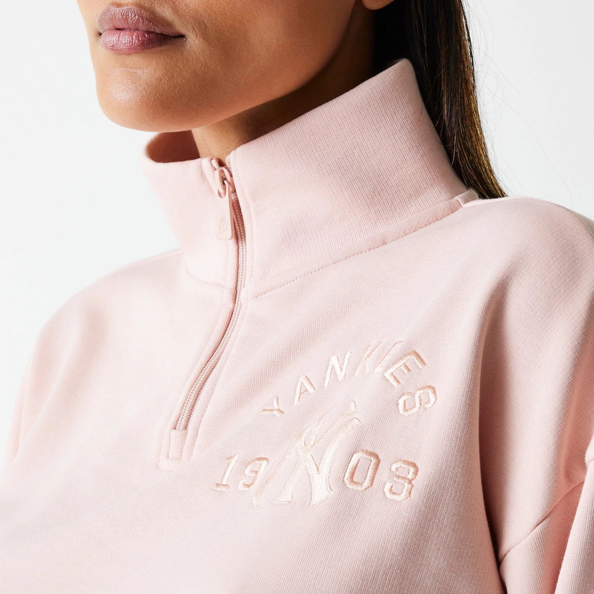 New Era New York Yankees Womens MLB Tonal Pastel Pink Cropped 1/4 Zip Sweater, close-up view on a model showing the high collar and pastel pink embroidered Yankees 1903 logo on the chest beside the quarter zip.