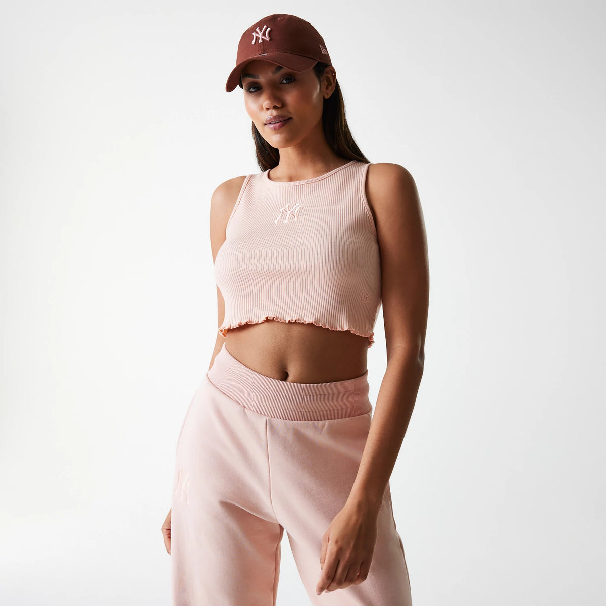 New Era New York Yankees Womens MLB Rib Pastel Pink Rib Tank Top, on-model view showing a white embroidered Yankees logo on the front, paired with pastel pink joggers and a brown cap with the Yankees logo and New Era flag logo.