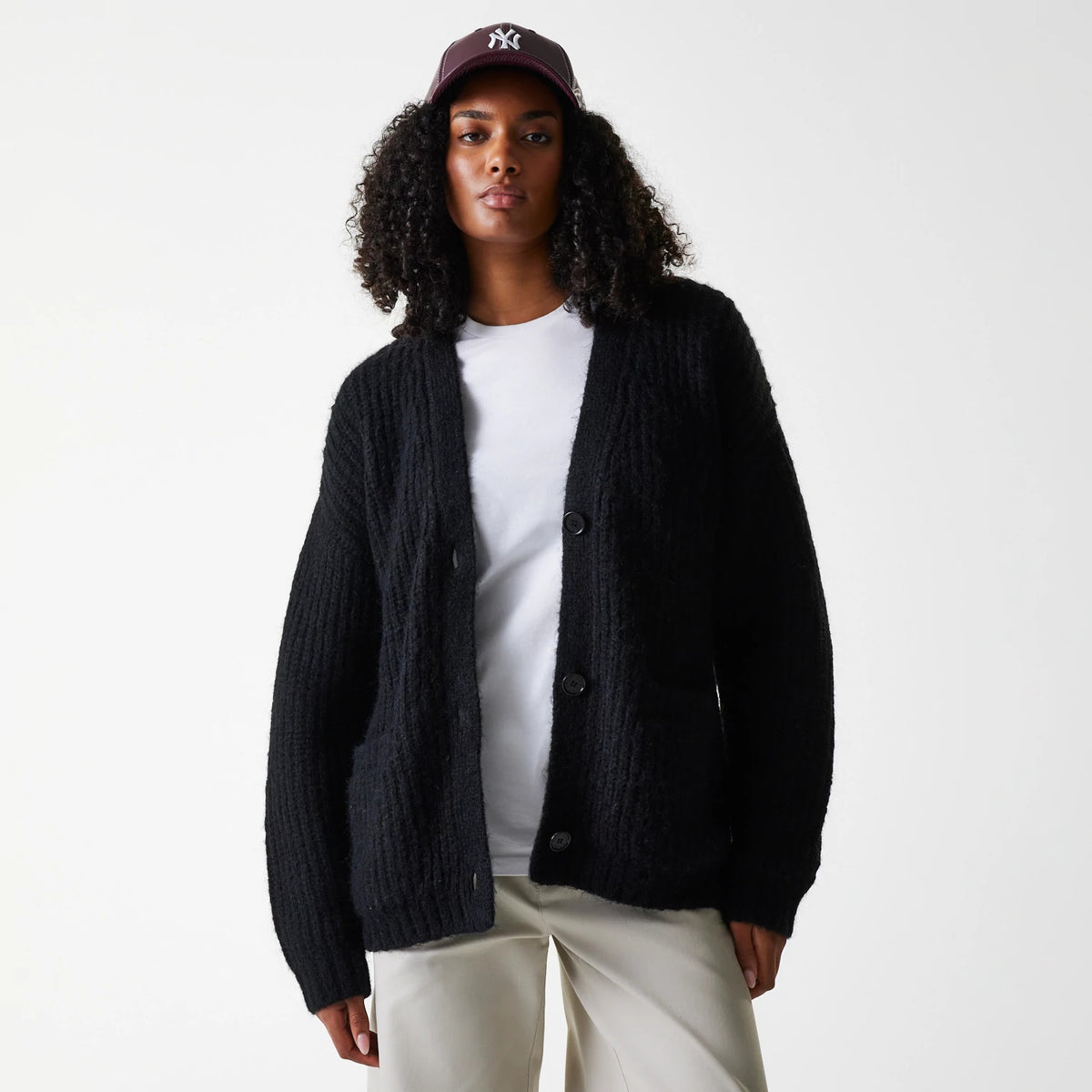 New Era New York Yankees Womens MLB Knit Black Cardigan, front view on a model wearing a white top and beige trousers, with a maroon cap sporting the Yankees logo in white embroidery.