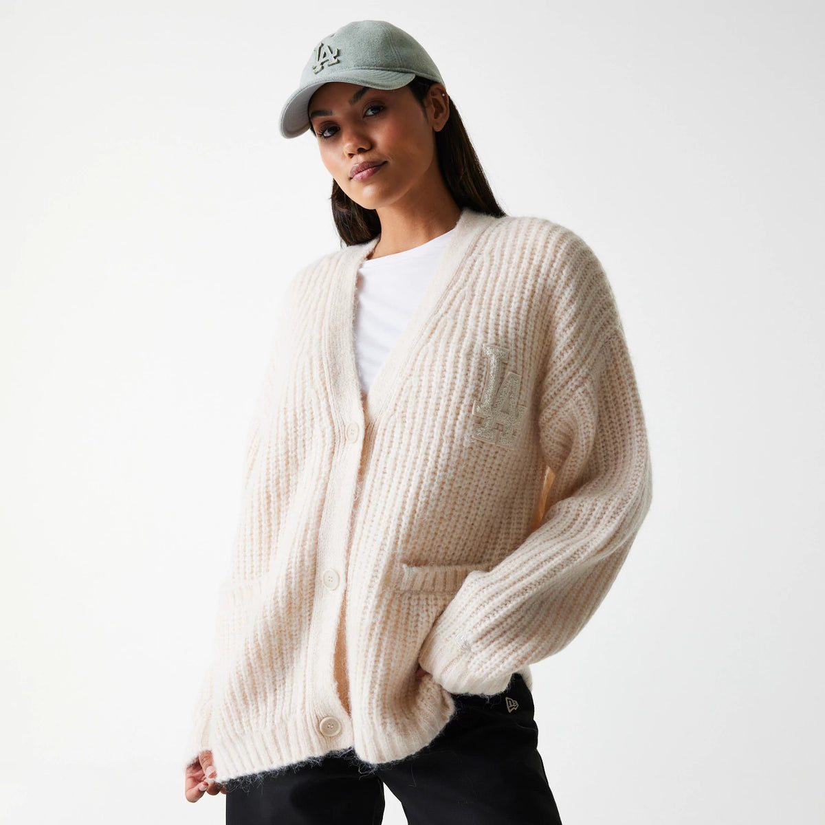 New Era LA Dodgers Womens MLB Knit Light Beige Cardigan, on a model with a grey LA Dodgers cap, featuring a textured cardigan design with buttoned front and embroidered LA logo on the left chest, complemented by black trousers.