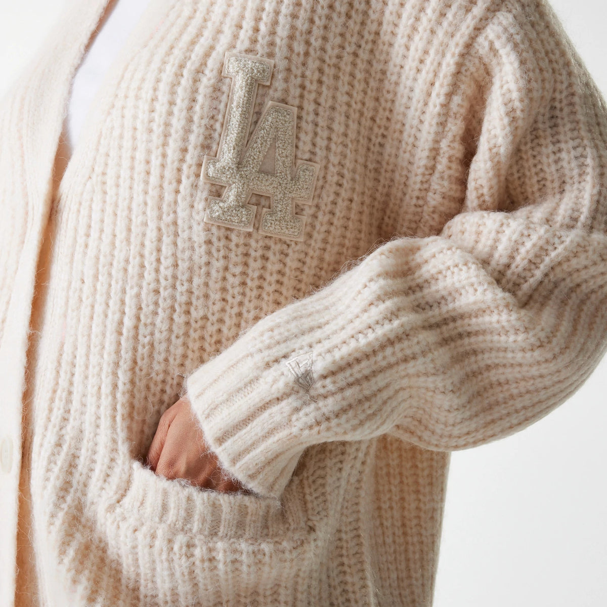 New Era LA Dodgers Womens MLB Knit Light Beige Cardigan, close-up view showing a textured design with a sparkling LA logo embroidered on the chest and ribbed cuffs, as well as a hand partly tucked into a front pocket.