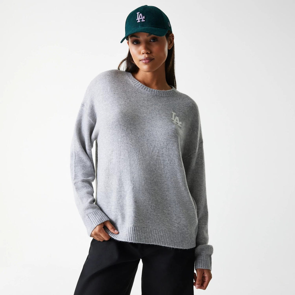 New Era LA Dodgers Womens MLB Knit Grey Crew Neck Sweater, front view on a model wearing a green cap, featuring the white LA logo embroidered on the left chest and a ribbed hem and cuffs.