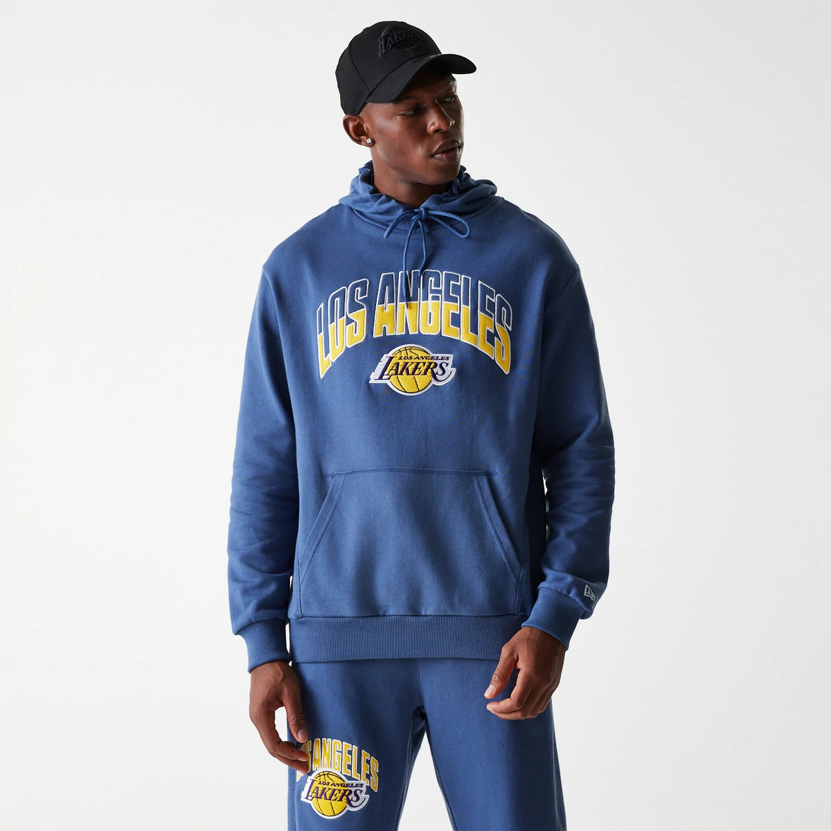 New Era LA Lakers NBA Arch Graphic Dark Blue Oversized Pullover Hoodie, on-model view showing the hood with drawstrings, large printed Los Angeles Lakers logo on the chest, and ribbed cuffs, paired with matching joggers.