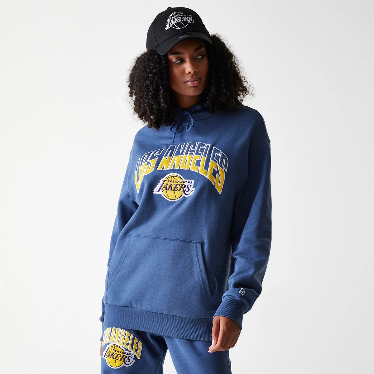 New Era LA Lakers NBA Arch Graphic Dark Blue Oversized Pullover Hoodie, on-model view showing a large Los Angeles Lakers logo across the chest, a kangaroo pocket at the front, and a small debossed New Era logo on the left wrist.