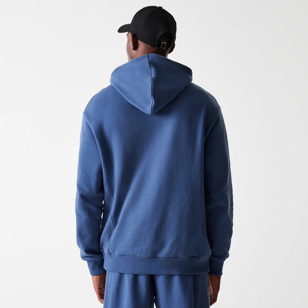 New Era LA Lakers NBA Arch Graphic Dark Blue Oversized Pullover Hoodie, rear view showing the deep blue fabric with a relaxed fit and a spacious hood, worn by a person in matching track pants and a black cap.