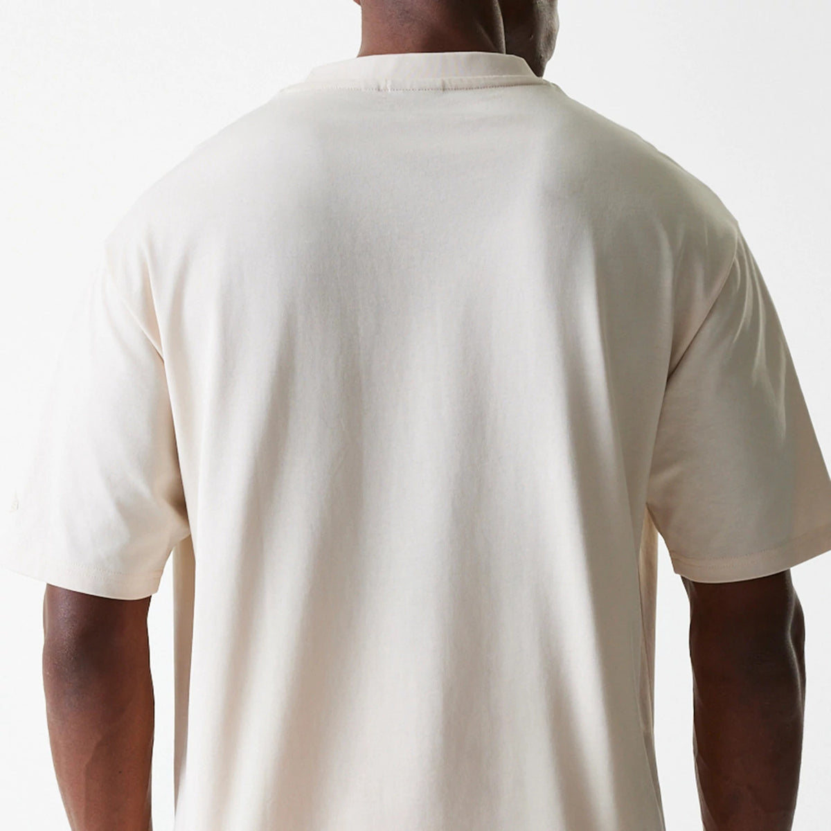 New Era Tech Light Beige Oversized T-Shirt, rear view showing the spacious cut of the light beige fabric draping over the shoulders and upper back, with short sleeves and a close-up of the neckline hem.
