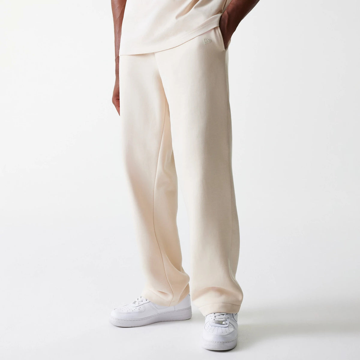 New Era Light Beige Straight Leg Joggers, on-model view showing a relaxed fit with side pockets and subtle New Era flag logo near the left pocket, styled with a matching light beige top and white trainers.