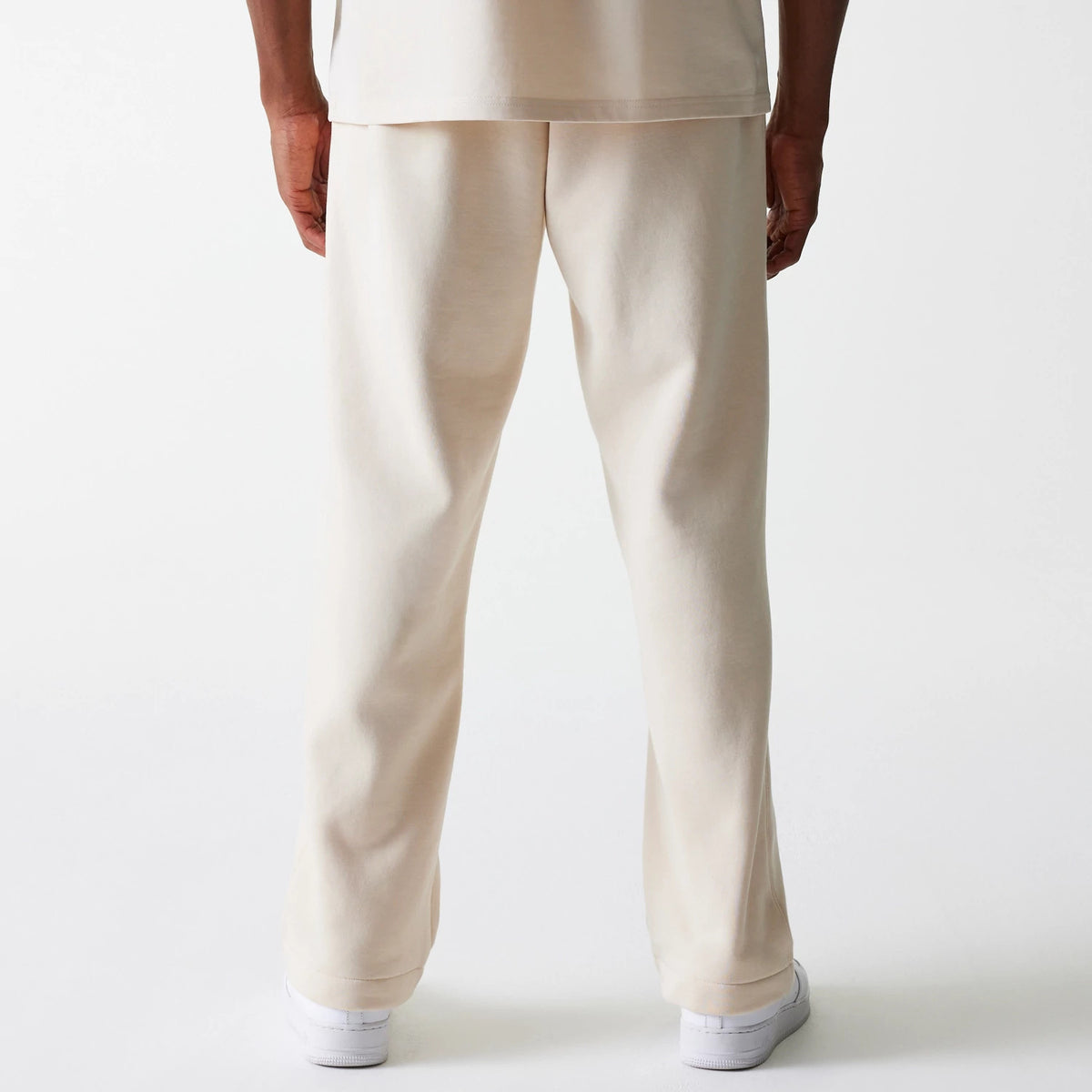 New Era Light Beige Straight Leg Joggers, rear view on a model wearing a matching light beige top and white trainers, showcasing the relaxed fit and minimalistic design at the back.