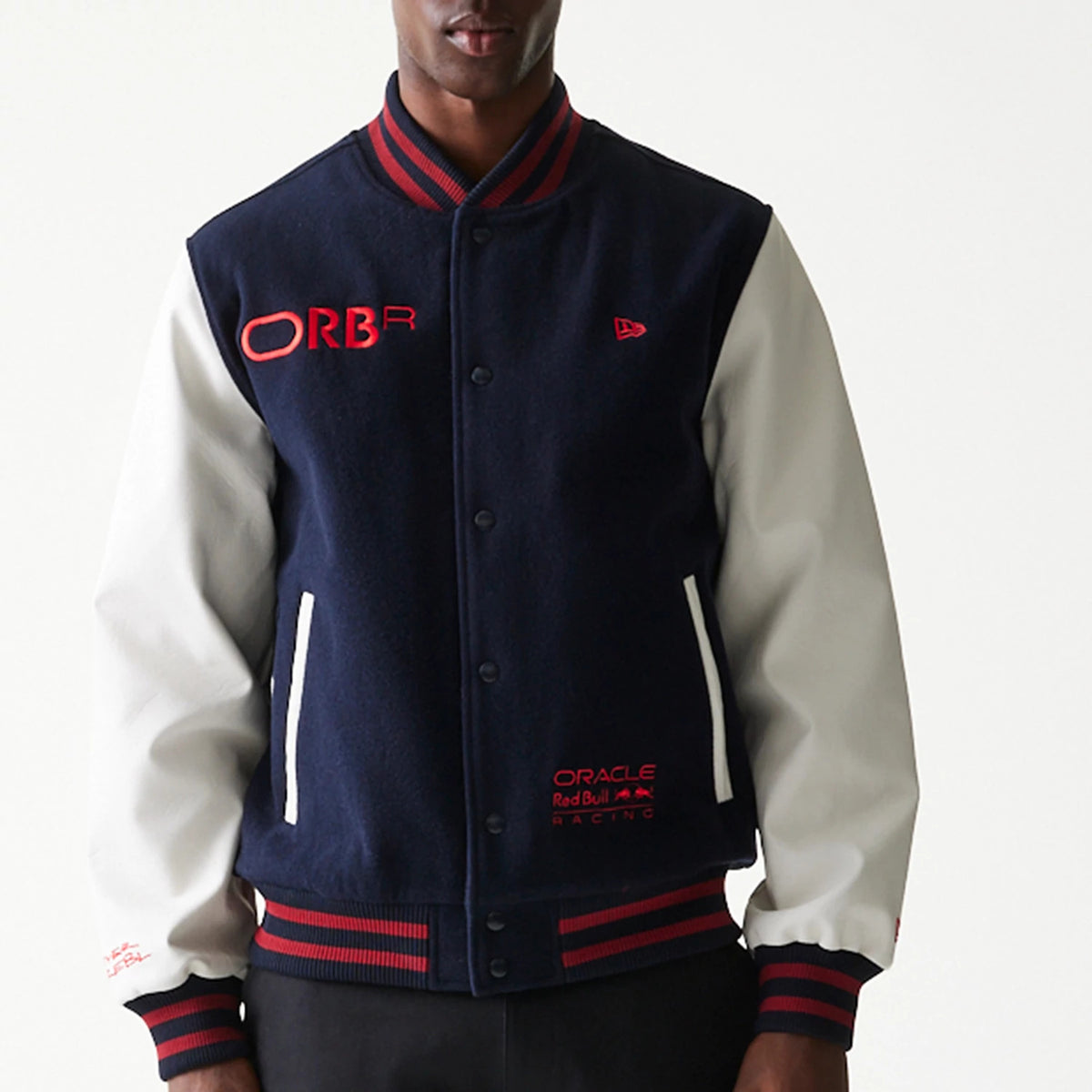 New Era Red Bull Racing Dark Blue Varsity Jacket, front view showing the dark blue body with white sleeves, embroidered ORBR logo in red on the chest, Oracle Red Bull Racing logo at the bottom, and striped red and blue collar and cuffs.