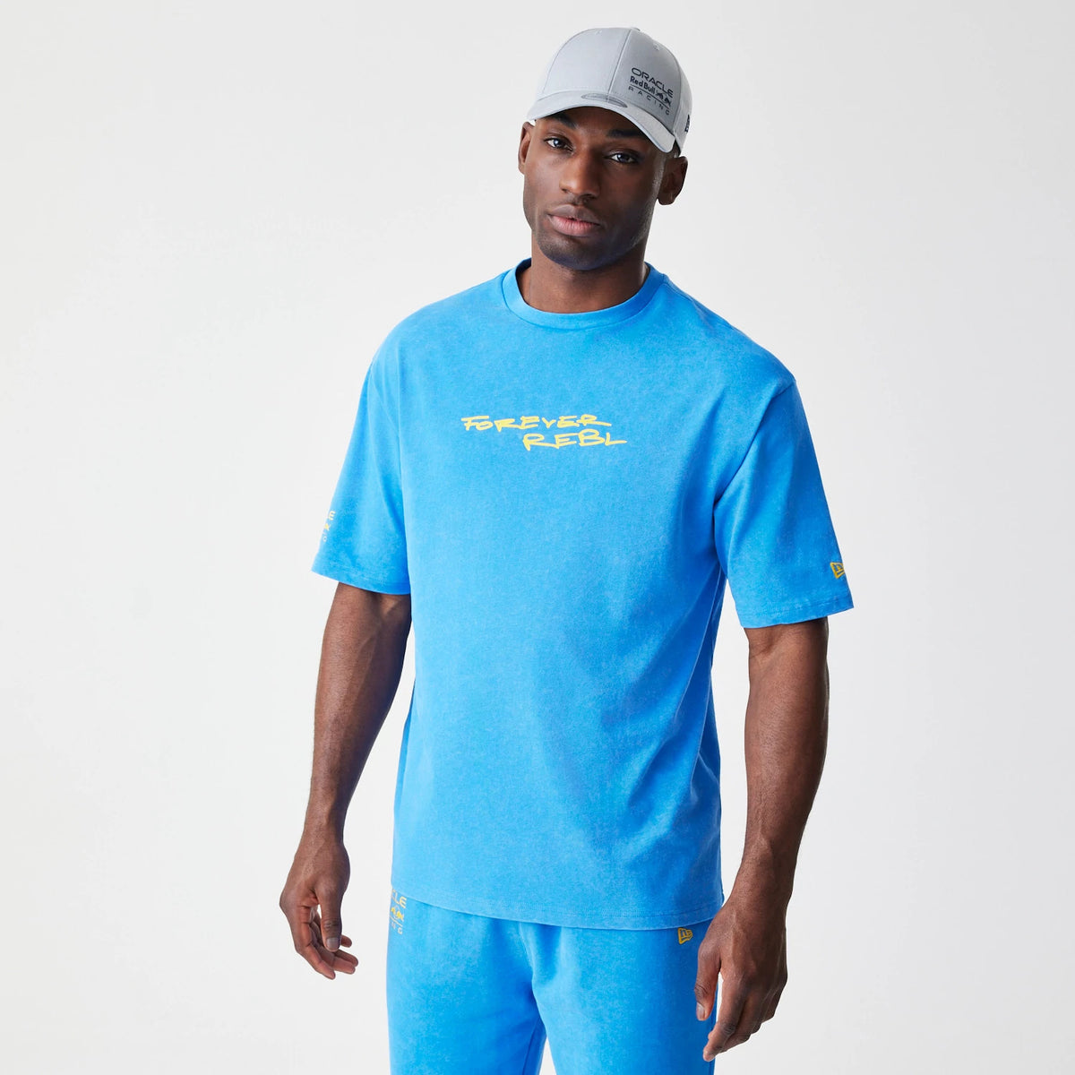 New Era Red Bull Racing Back Graphic Blue Oversized T-Shirt, front view on-model featuring a yellow printed Forever Rebel graphic across the chest, with New Era and Red Bull Racing logos on the sleeve.