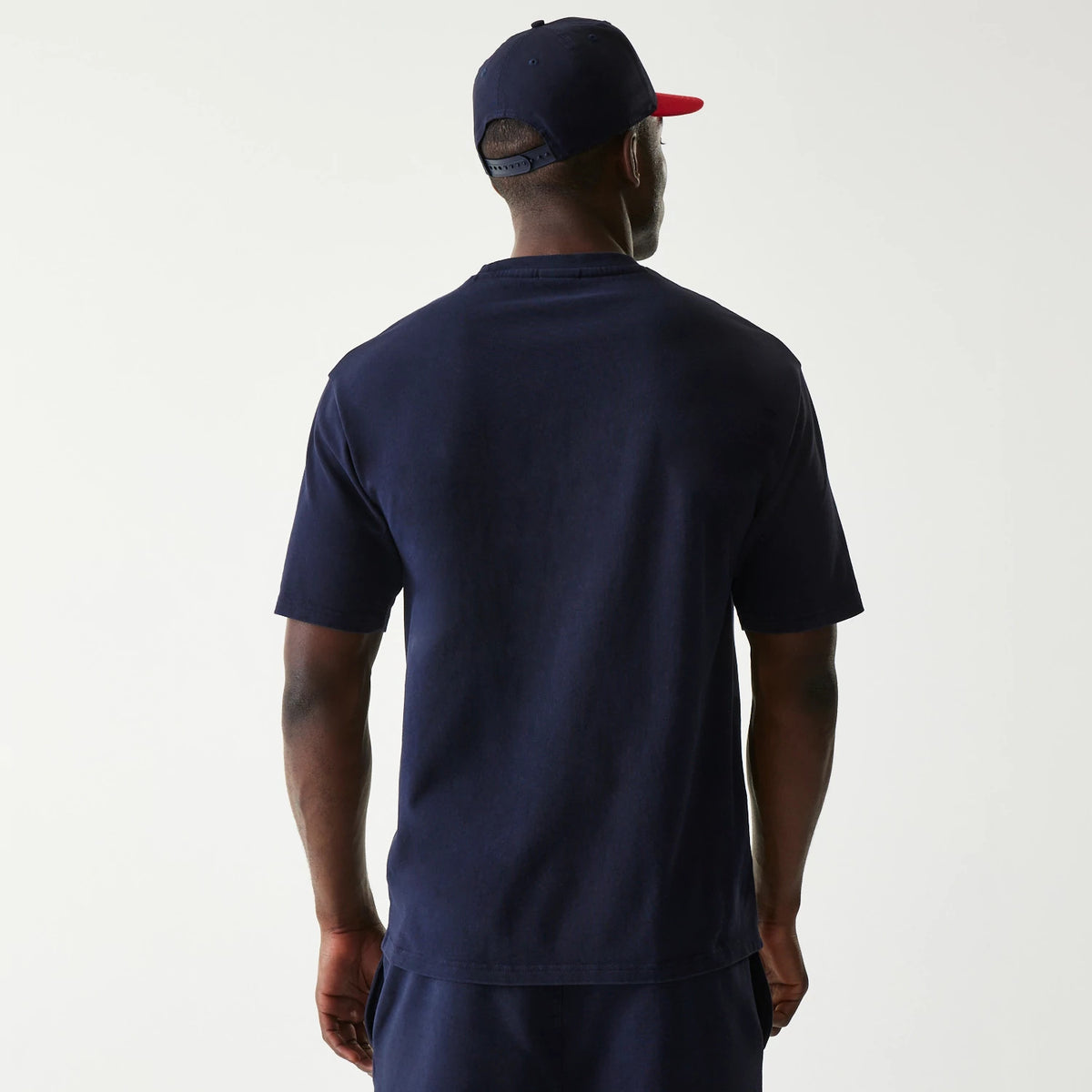 New Era Red Bull Racing Dark Blue Oversized T-Shirt, back view on-model showing the plain dark blue canvas with no additional graphics, complemented by a matching cap with a contrasting red visor.