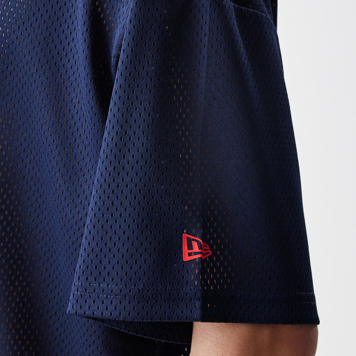 New Era Red Bull Racing Graphic Mesh Dark Blue Oversized T-Shirt, side view showing the sleeve with a red embroidered New Era logo near the hem, and the mesh design clearly across the dark blue fabric.