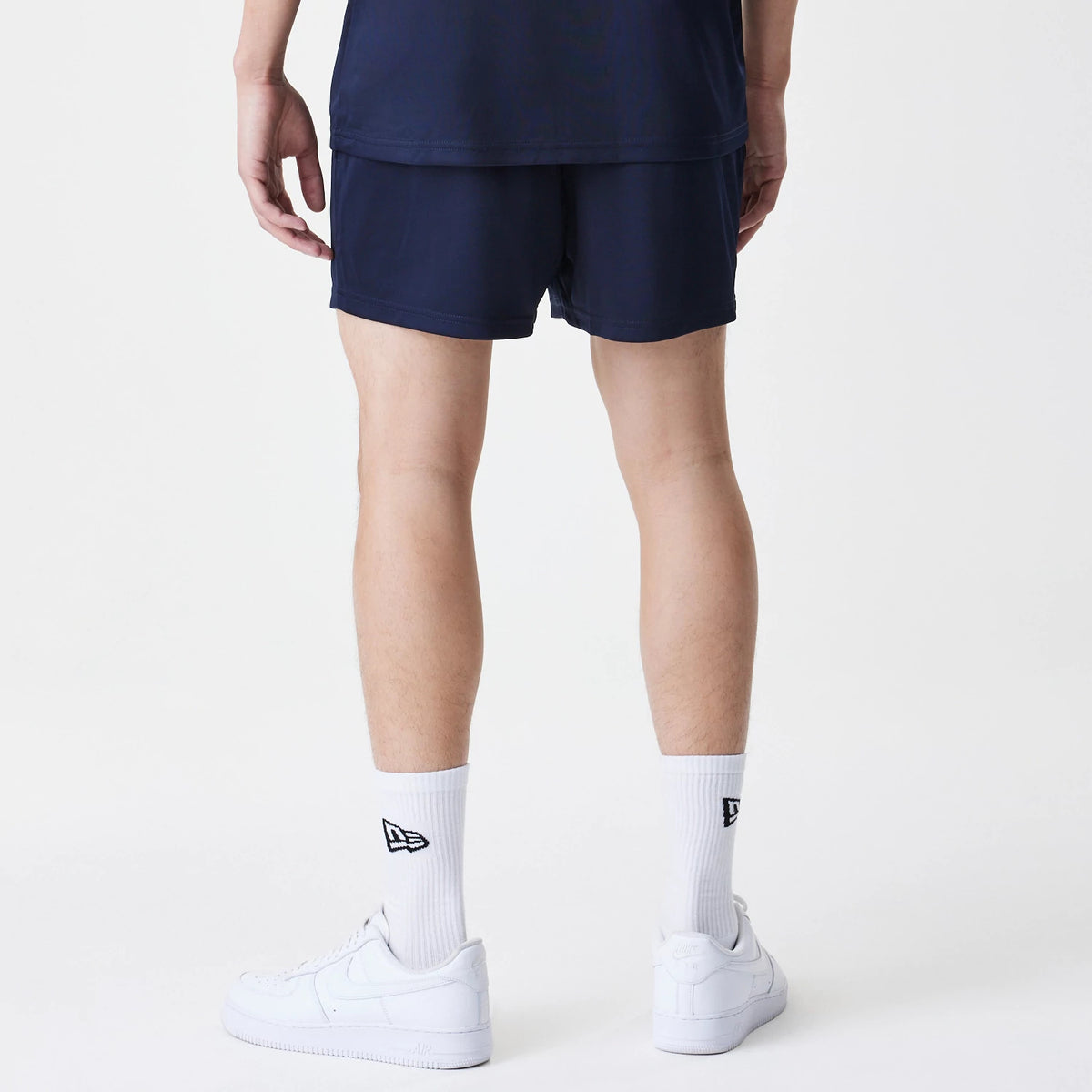 New Era Red Bull Racing Graphic Dark Blue Football Shorts, back view on-model displaying the plain dark blue design, styled with white trainers and socks featuring a black embroidered New Era logo.