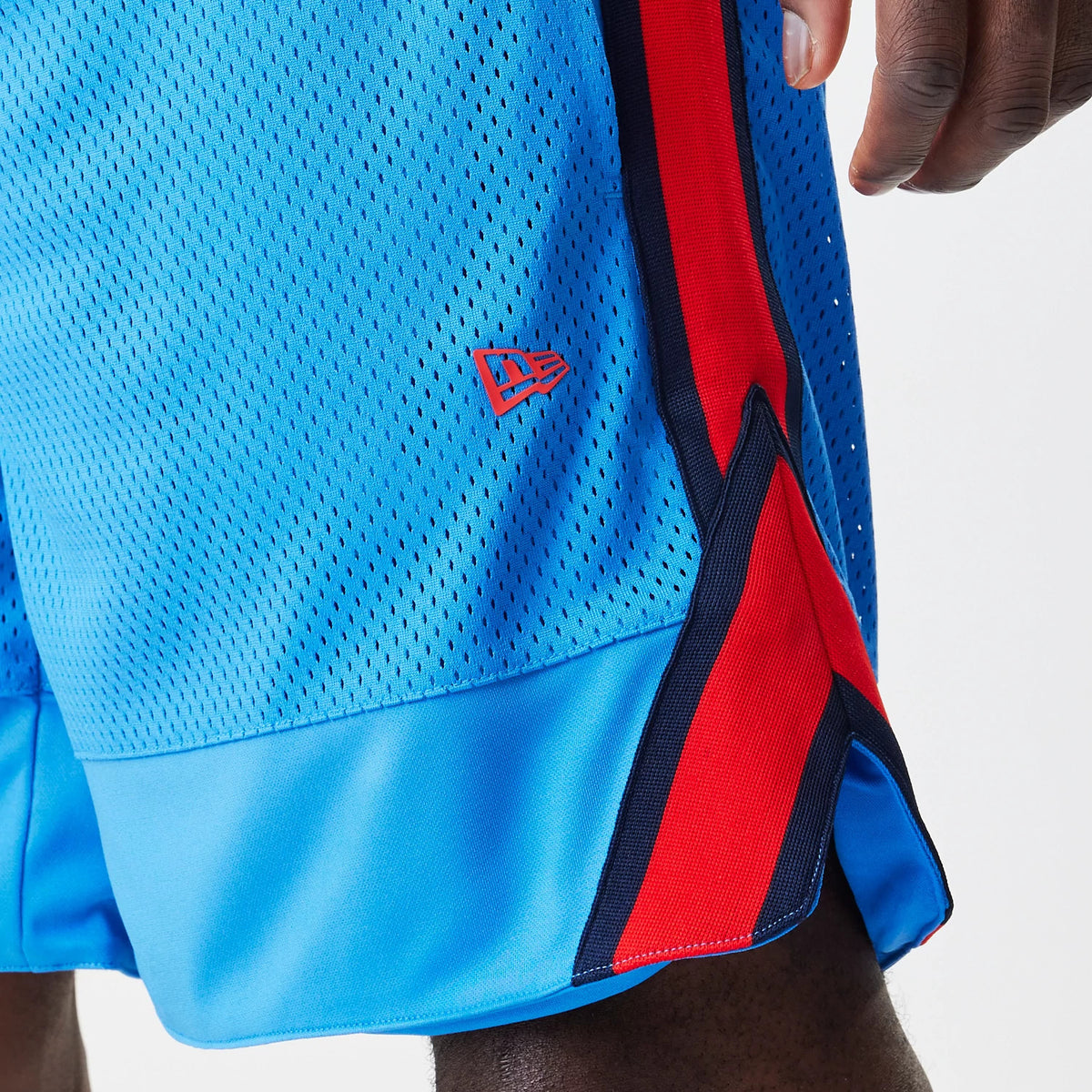 New Era Red Bull Racing Basketball Mesh Blue Shorts, three-quarter view showing a close-up of the blue mesh fabric with red and black side panels, a small red embroidered New Era logo near the hem, worn by a model.