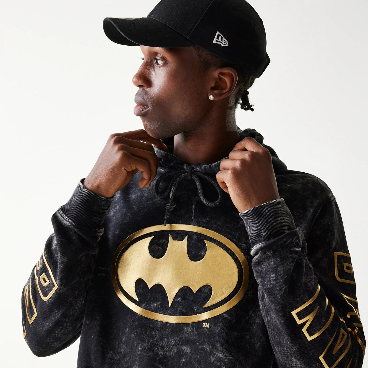 New Era Batman 1989 Black Pullover Hoodie, front view on-model showing a large gold Batman logo centred on the chest, gold lettering along the sleeve, and a drawstring hood worn visibly around the neck.