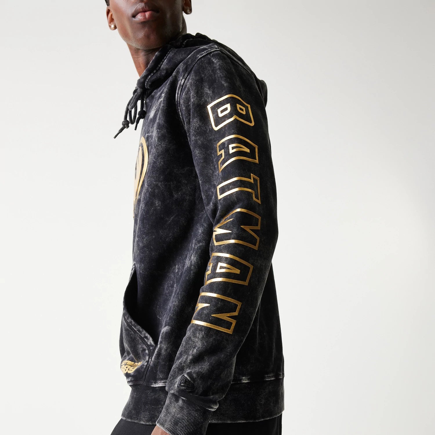 New Era Batman 1989 Black Pullover Hoodie, three-quarter view showing the BATMAN lettering in gold printed down the right sleeve, with a drawstring hood and a kangaroo pocket at the front.