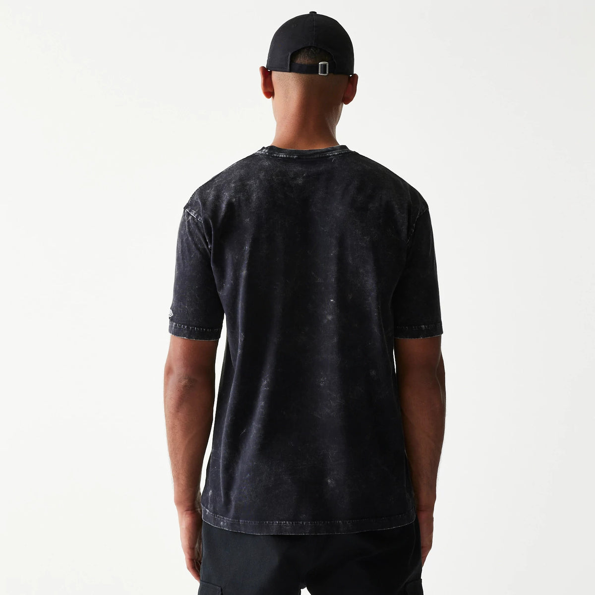 New Era Batman 1989 Black T-Shirt, back view on a model wearing a black cap, showing a faded black fabric with short sleeves and an embroidered New Era logo near the hem on the sleeve.