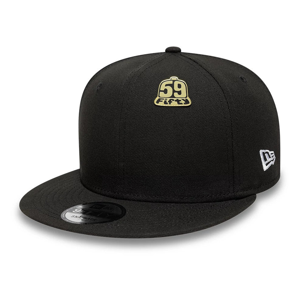 New Era 59FIFTY Day Cap Gold Pin Badge, front view showing the structured black crown with a gold embroidered 59FIFTY badge centred above the visor, and a white embroidered New Era logo on the left side.