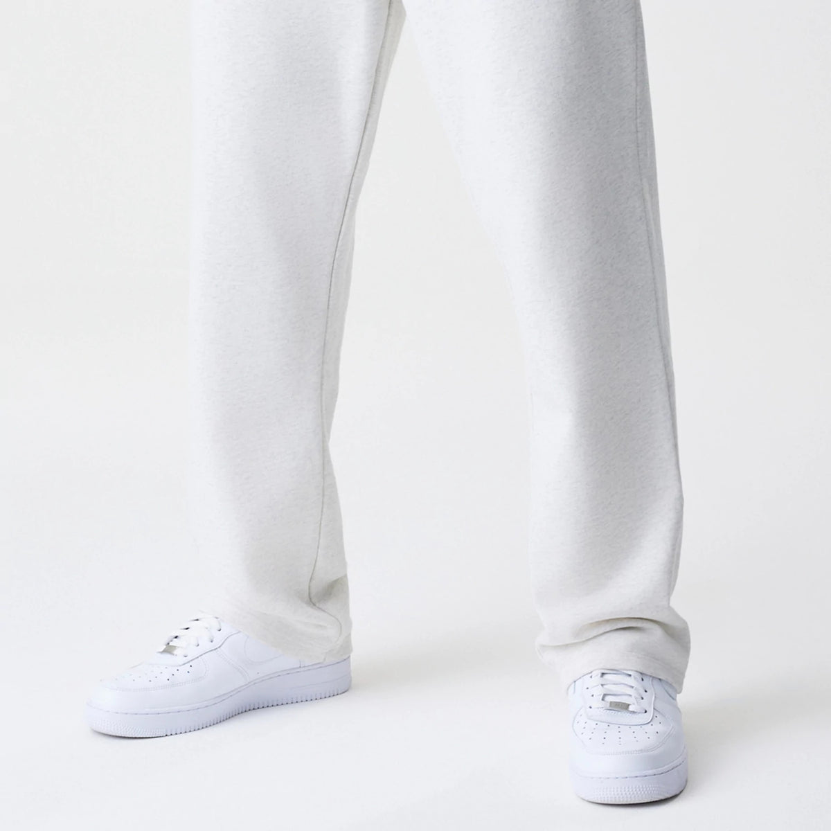 New Era Premium Essential Pastel Grey Joggers, front view on a model displaying the relaxed fit and texture of the pastel grey fabric, paired with white trainers for a casual look.