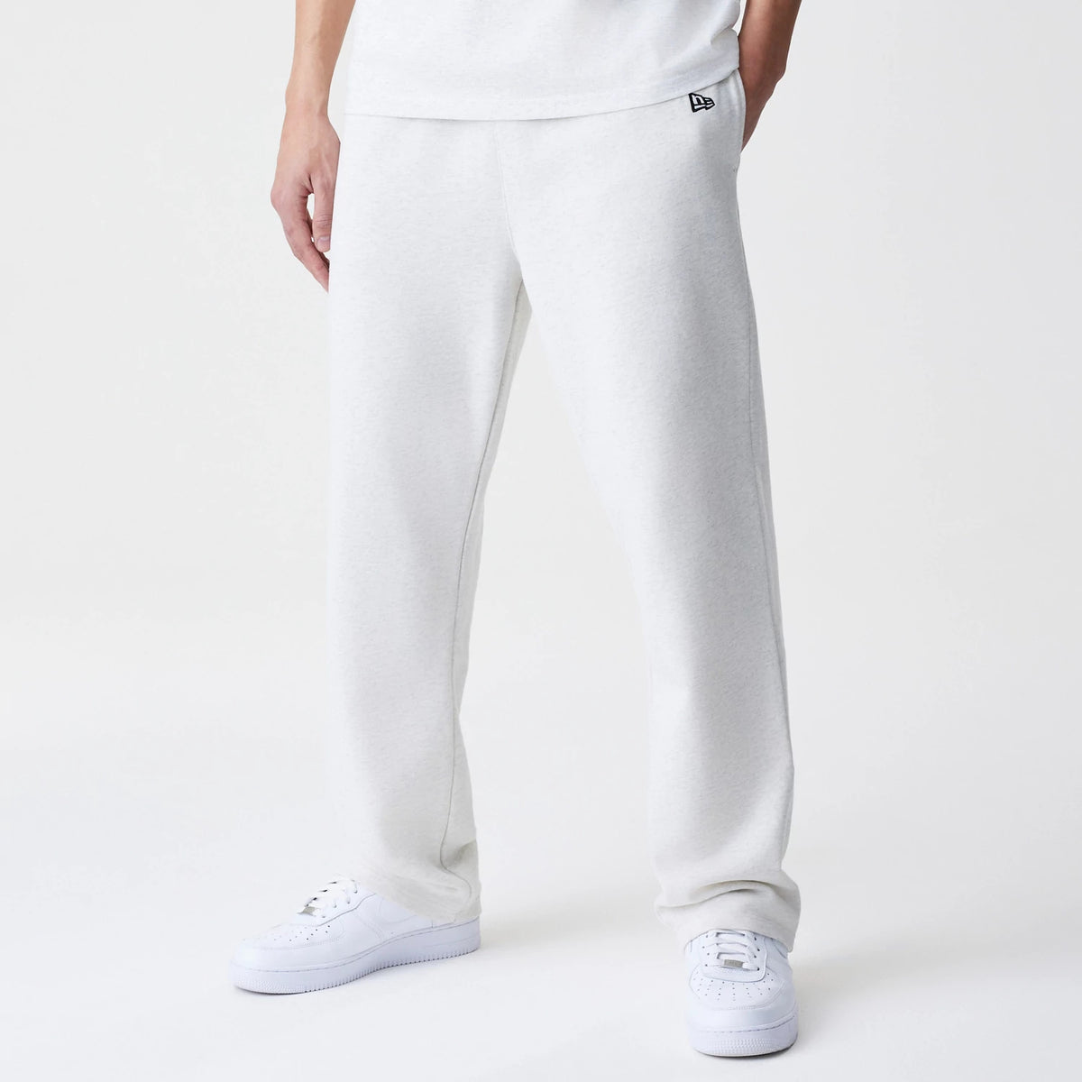 New Era Premium Essential Pastel Grey Joggers, front view on-model showing the black New Era flag logo on the upper left thigh, with a relaxed fit and elastic waistband, paired with white trainers.