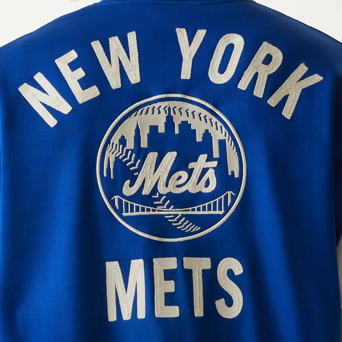New Era New York Mets MLB Jersey Blue Bomber Jacket, back view featuring large embroidered New York Mets logo centred on a royal blue background with white lettering above and below.