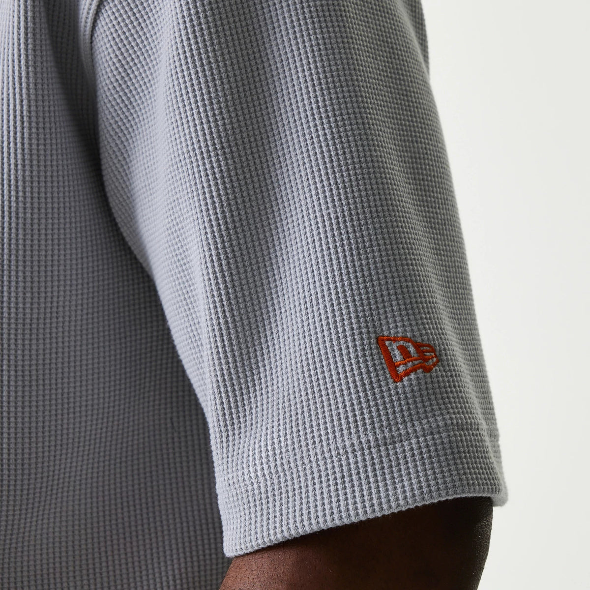 New Era New York Mets MLB Waffle Grey Oversized T-Shirt, side view showing the textured waffle pattern fabric on the sleeve and a small embroidered orange New Era logo near the hem, providing a branded detail.