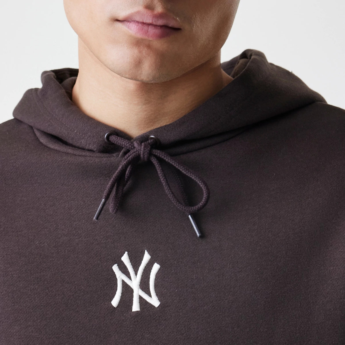 New Era New York Yankees MLB Midi League Essential Dark Brown Oversized Pullover Hoodie, front view on-model showing the small white embroidered Yankees logo on the chest below the drawstring hood.