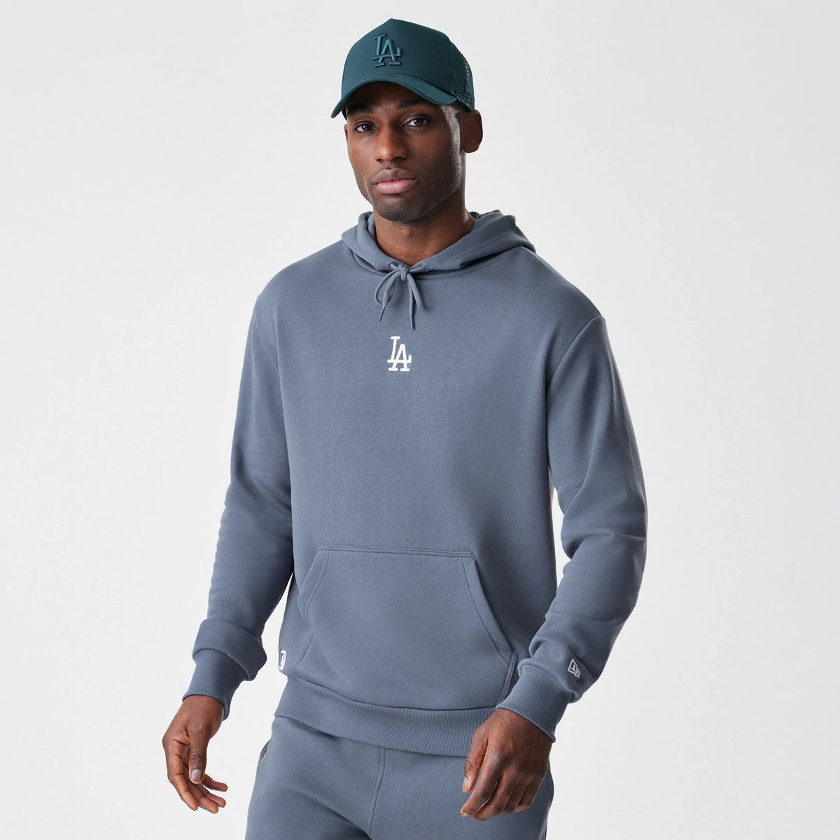 New Era LA Dodgers MLB Midi League Essential Dark Grey Oversized Pullover Hoodie, front view on-model showing the white embroidered LA logo on the chest, drawstring hood, kangaroo pocket, and New Era logo on the sleeve.