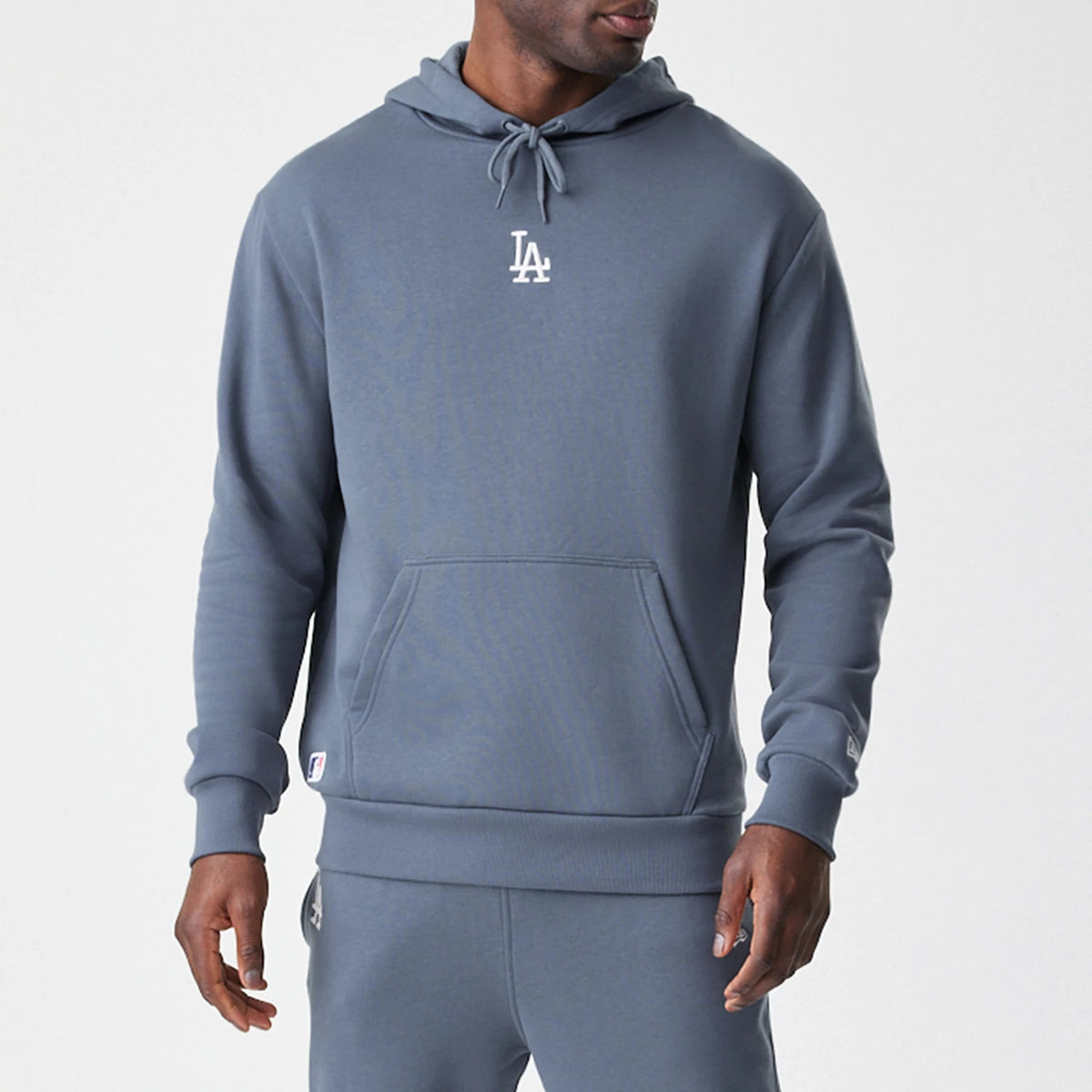 New Era LA Dodgers MLB Midi League Essential Dark Grey Oversized Pullover Hoodie, front view showing a white embroidered LA logo centred on the chest, a matching drawstring hood, and a kangaroo pocket, styled casually by a model.