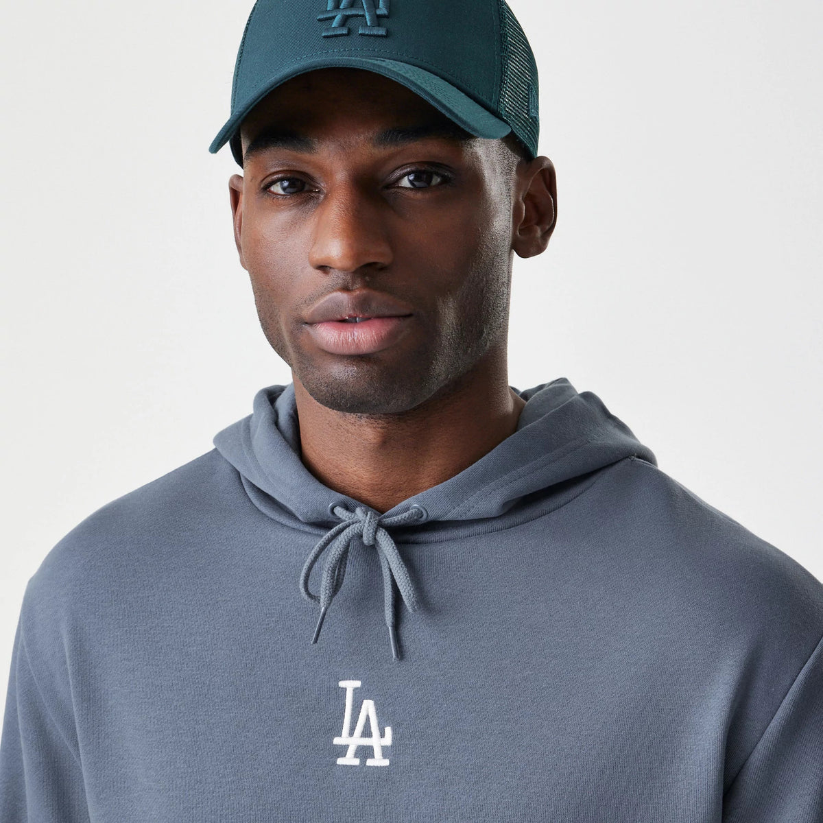 New Era LA Dodgers MLB Midi League Essential Dark Grey Oversized Pullover Hoodie, front view on-model showing the LA Dodgers raised logo embroidered in white on the chest with a drawstring hood and a matching cap worn above.