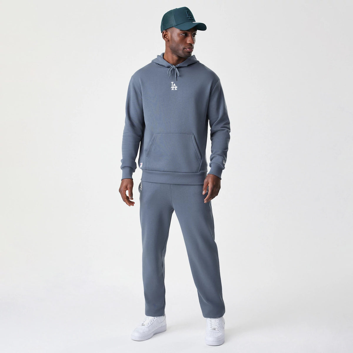 New Era LA Dodgers MLB Midi League Essential Dark Grey Oversized Pullover Hoodie, front view on-model featuring a white embroidered LA logo centred on the chest, drawstring hood, and kangaroo pocket, styled with matching dark grey trousers.