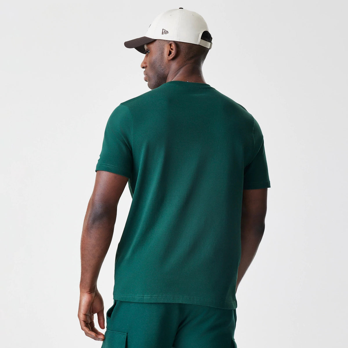 New Era LA Dodgers MLB Script Graphic Dark Green T-Shirt, back view on a model paired with dark green shorts and a beige cap, showing the solid dark green colour of the short sleeves and back with no graphics or logos.
