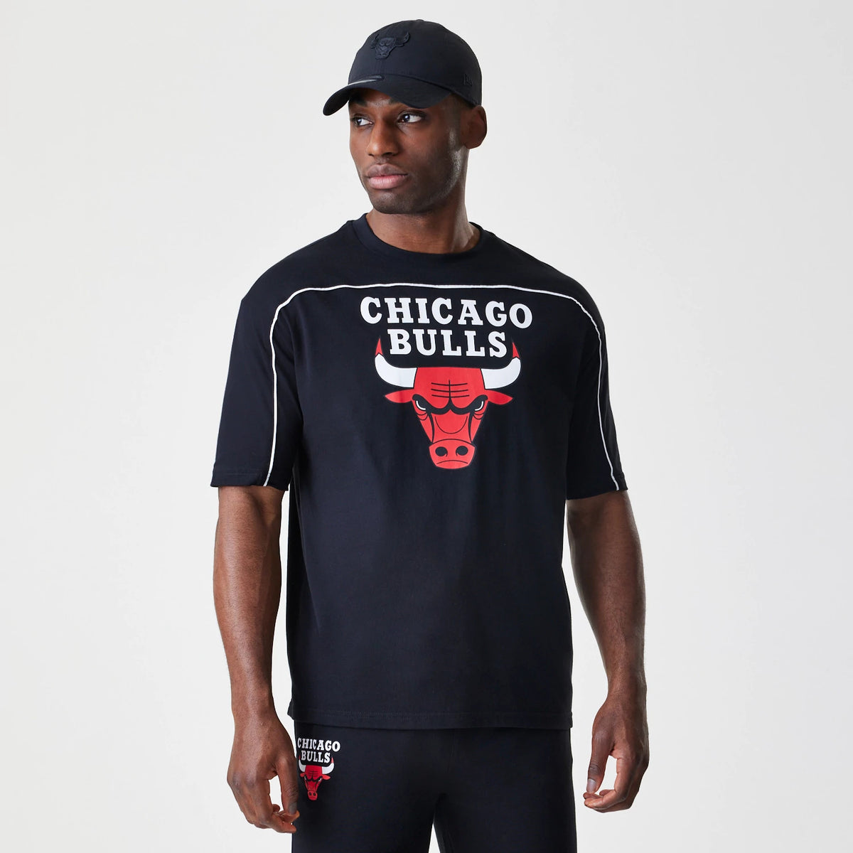 New Era Chicago Bulls NBA Piping Stripe Black Oversized T-Shirt, front view on-model showing the red Bulls logo and CHICAGO BULLS lettering across the chest, with contrasting white piping along the shoulders and sleeves.