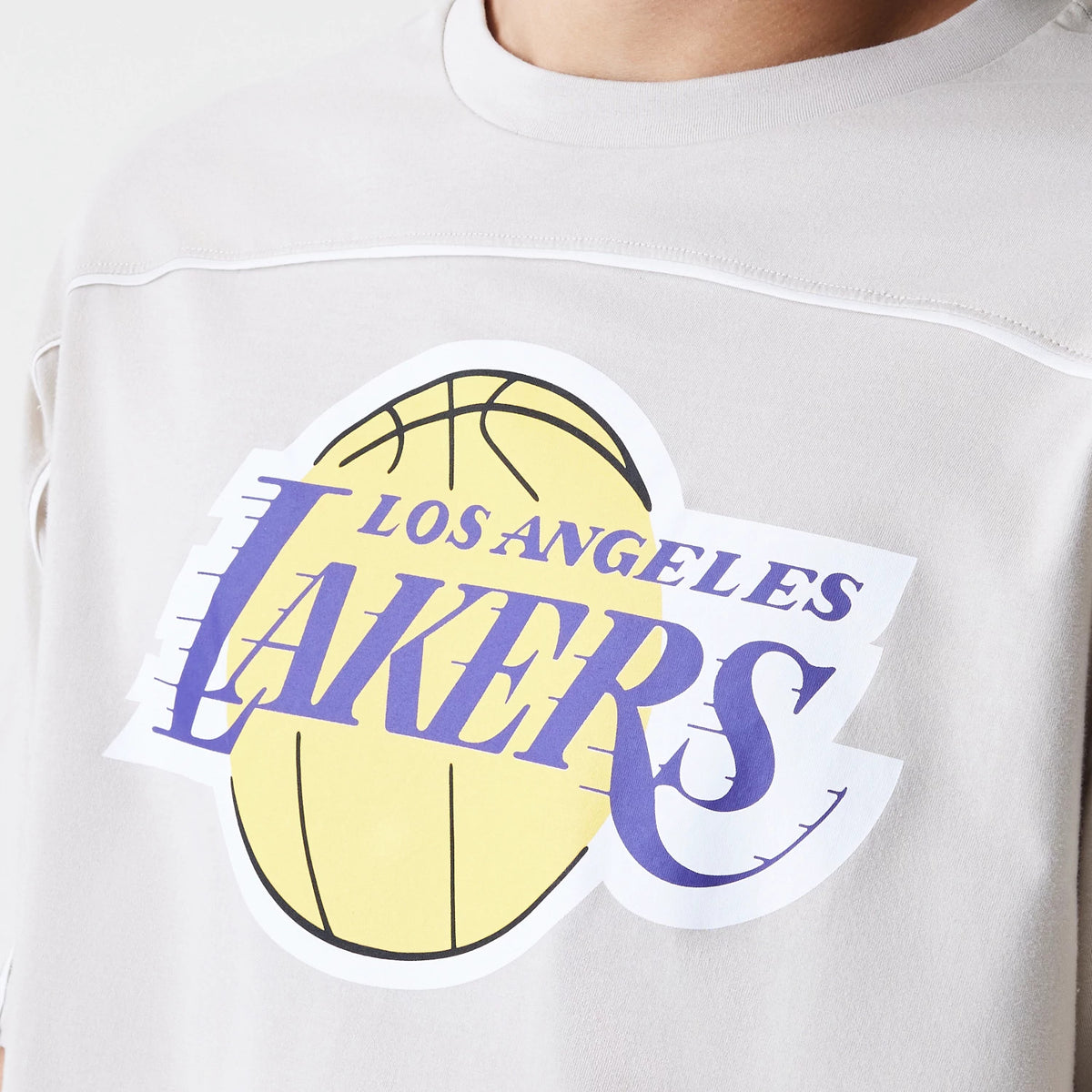 New Era LA Lakers NBA Piping Light Beige Oversized T-Shirt, front view displaying a prominent printed Lakers logo with a basketball design on the chest, worn by a model, featuring piping detail across the shoulder.