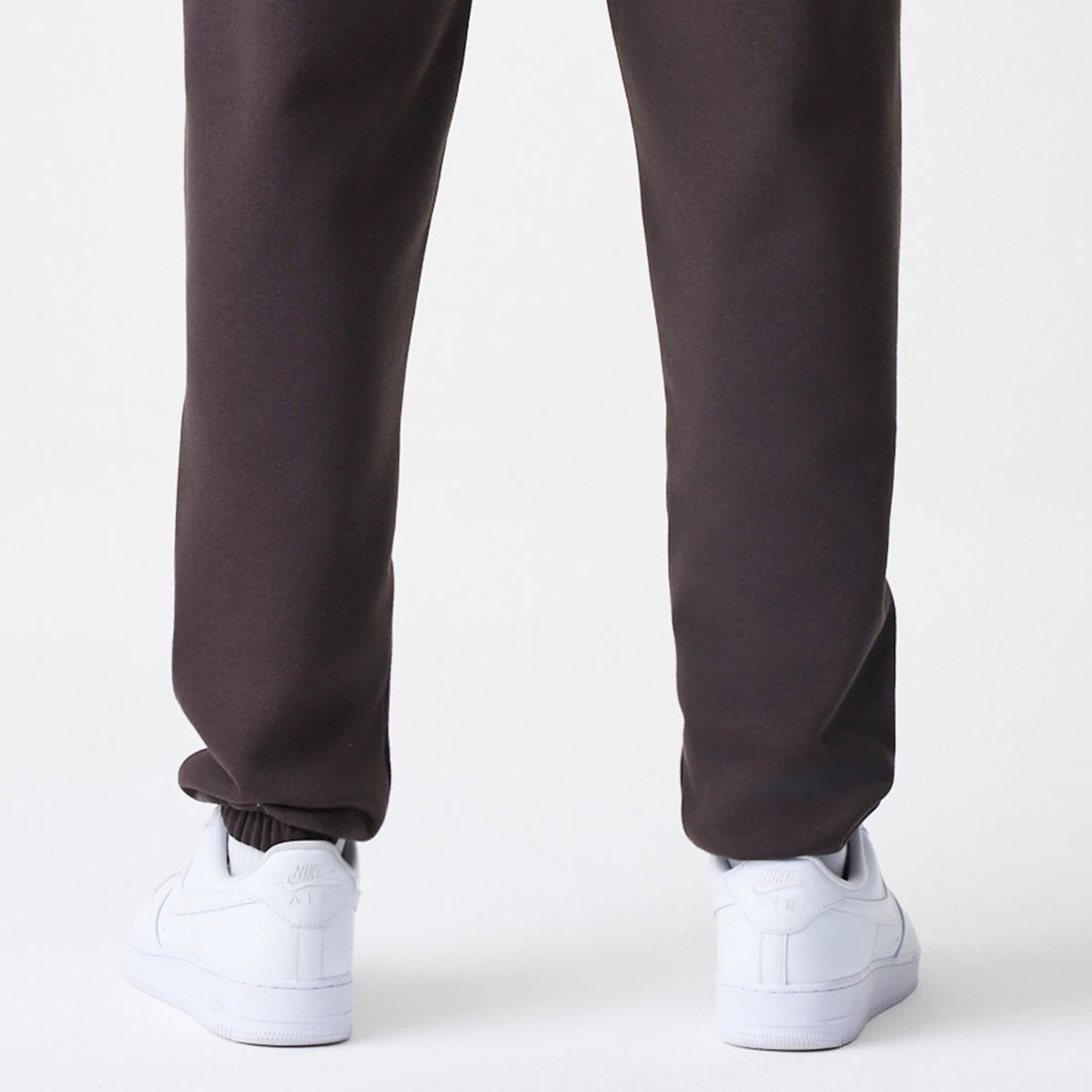 New Era New York Yankees MLB Midi League Essential Dark Brown Joggers, rear view on a model showing the relaxed fit with ribbed cuffs above white sneakers, highlighting the dark brown fabric.