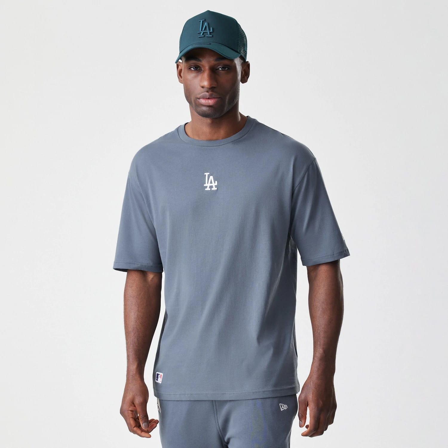 New Era LA Dodgers MLB Midi League Essential Dark Grey Oversized T-Shirt, front view on-model showing a white embroidered LA logo on the chest, styled with a matching dark cap featuring a raised LA logo.