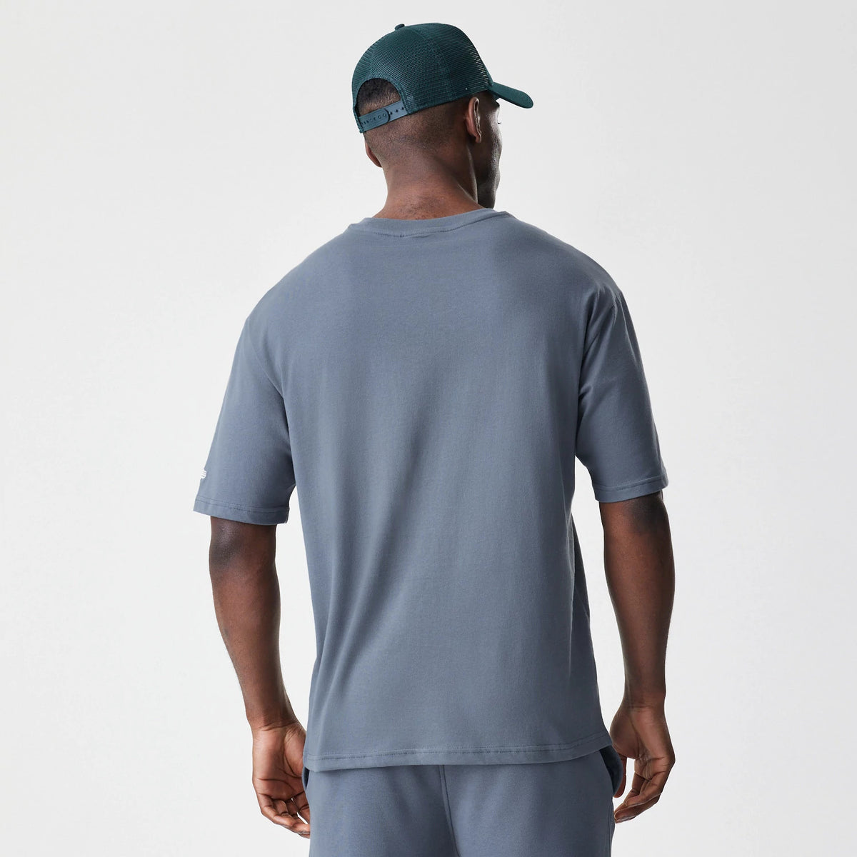 New Era LA Dodgers MLB Midi League Essential Dark Grey Oversized T-Shirt, back view on a model wearing a cap, showing the plain dark grey back with a relaxed fit and short sleeves extending to the elbows.