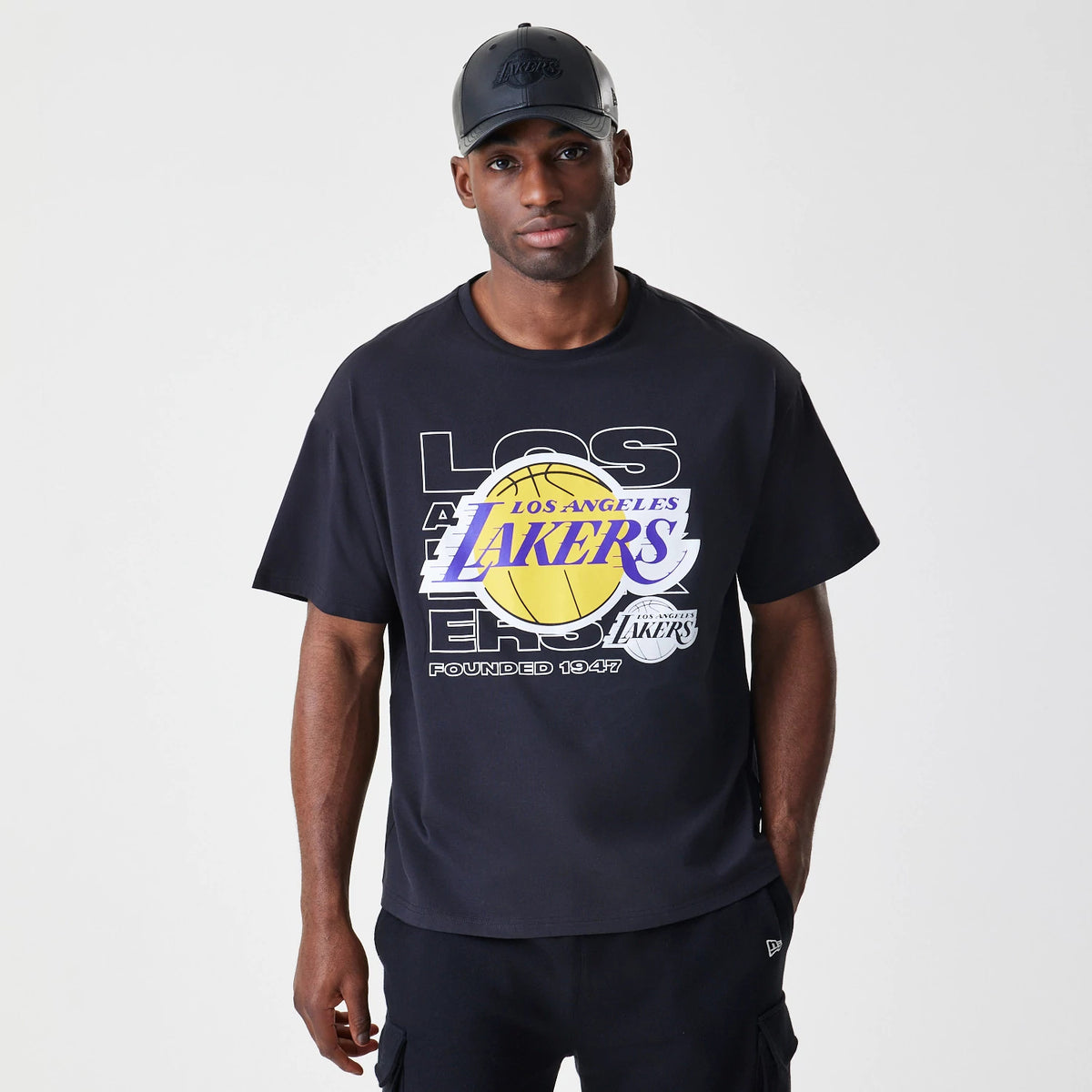 New Era LA Lakers NBA Outline Graphic Navy Oversized T-Shirt, front view on a model showcasing a large printed Lakers logo in yellow and purple across the chest with LOS ANGELES text behind and a New Era logo on the left sleeve.