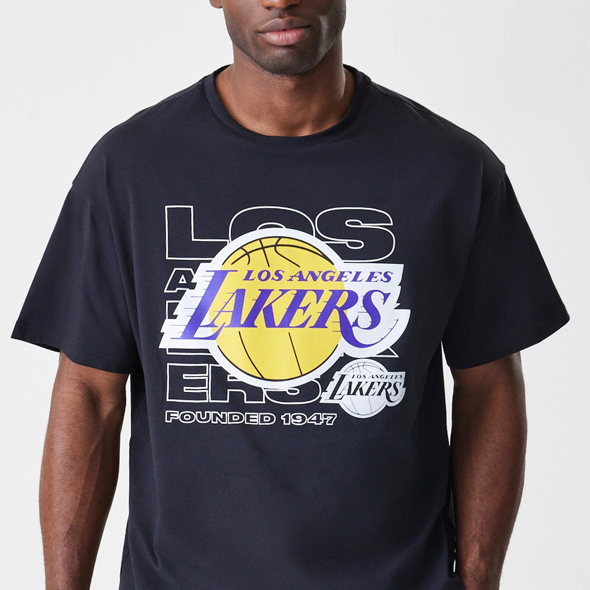 New Era LA Lakers NBA Outline Graphic Navy Oversized T-Shirt, front view on-model featuring a large printed yellow basketball graphic with purple Lakers lettering across the chest, and the phrase Founded 1947 in white below.