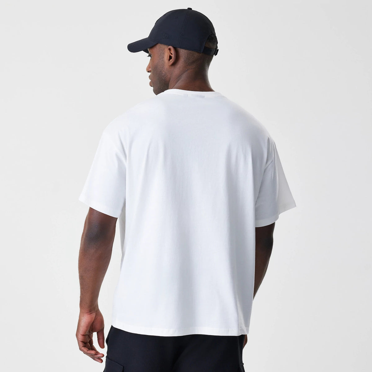 New Era Chicago Bulls NBA Outline Graphic White Oversized T-Shirt, back view on a model wearing a dark cap, showing the plain white back of the T-shirt with a relaxed fit and dropped shoulders.