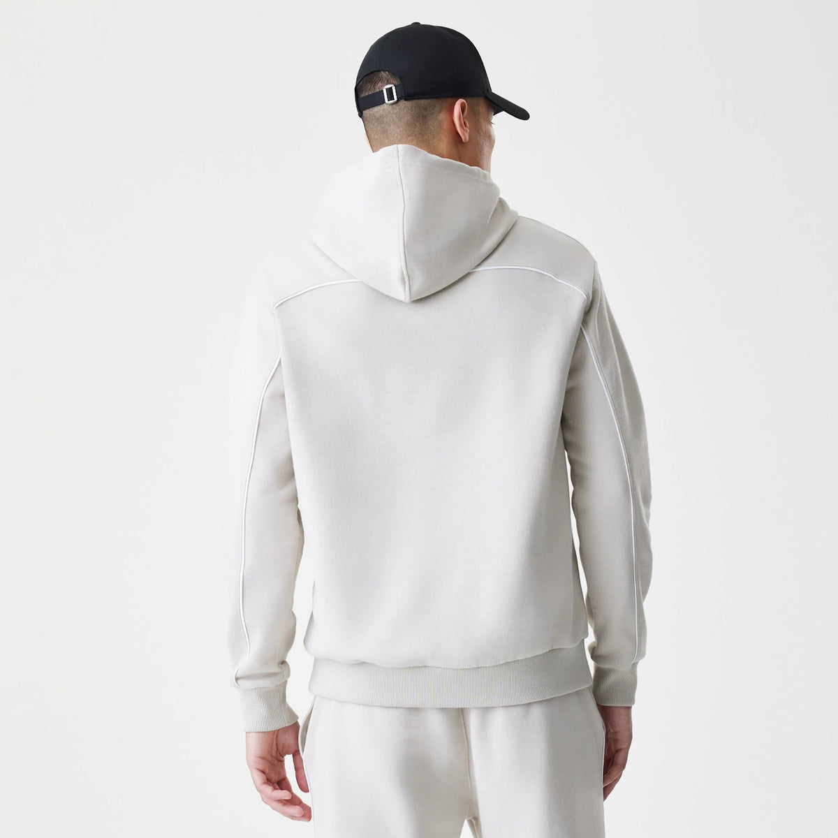 New Era LA Lakers NBA Piping Cream Oversized Pullover Hoodie, back view on a model wearing matching cream trousers and a black cap, showing the hoodie with piping detail along the shoulders and sleeves.