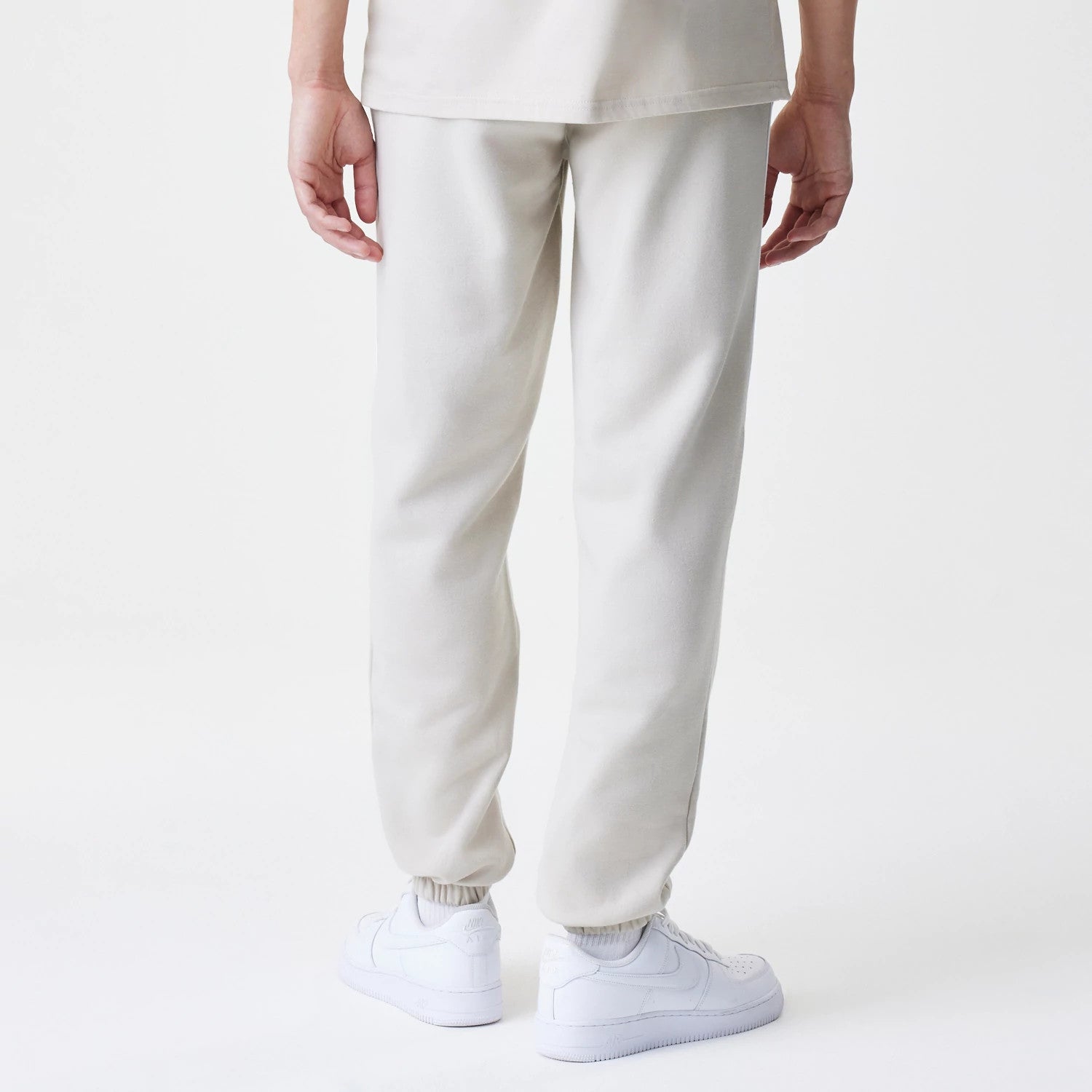 New Era LA Lakers NBA Piping Cream Joggers, rear view showing the elasticated cuffs and cream fabric of the relaxed fit joggers, with simple styling emphasized by white trainers and a top.