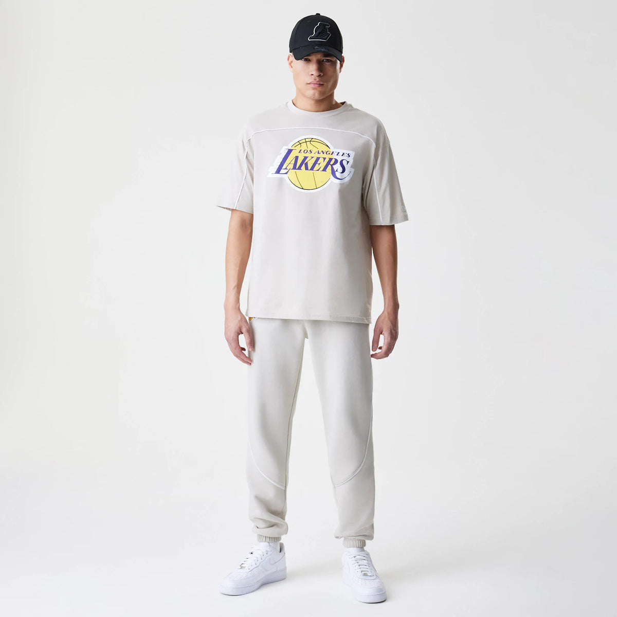 New Era LA Lakers NBA Piping Cream Joggers, front view on a model with a matching T-shirt and white trainers, showing a relaxed fit with piped on the front and ribbed cuffs at the ankles.